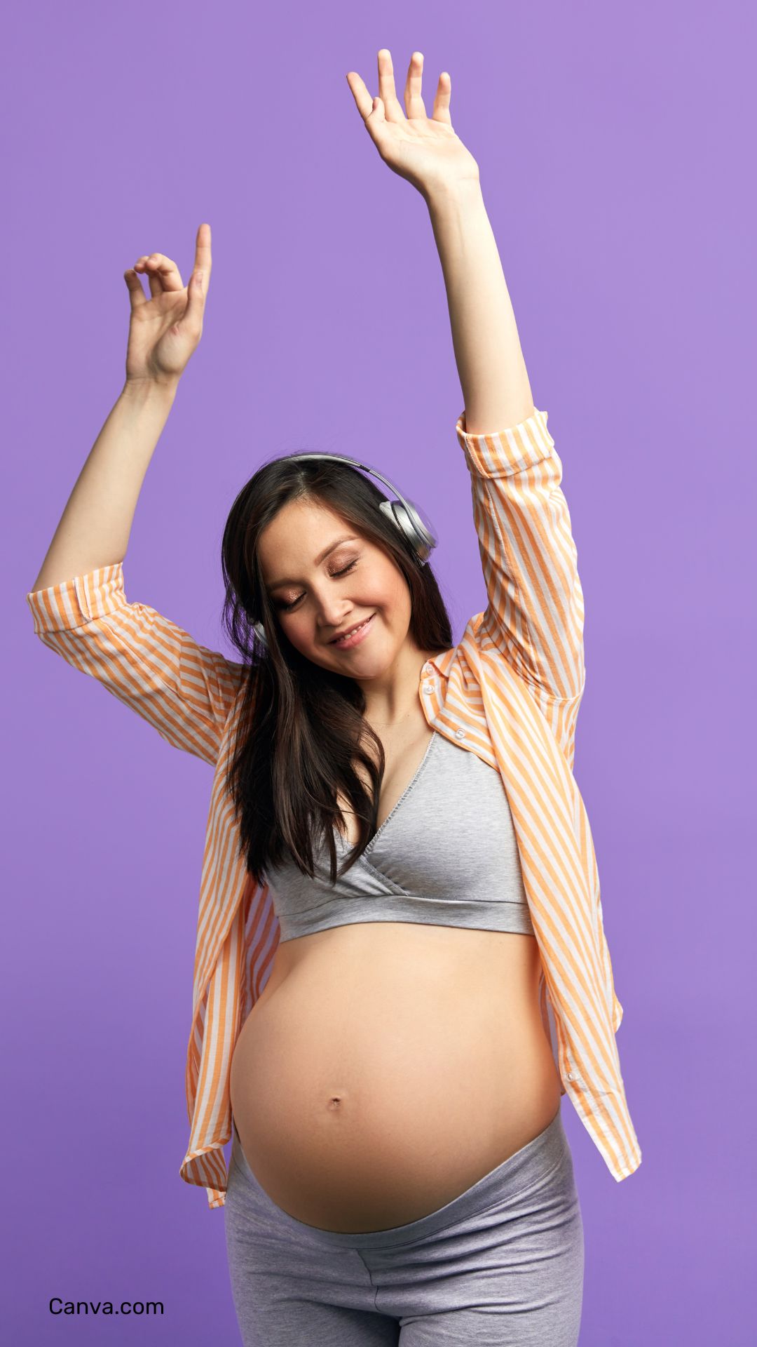 femme enceinte souriant en écoutant de la musique et levant les bras au ciel