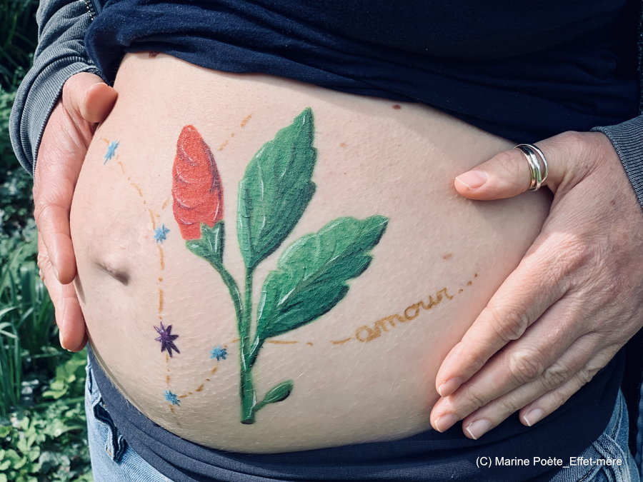 Photo d'un ventre de femme enceinte avec peinture corporelle éphémère représentant une fleur en bourgeon et des étoiles et le mot amour