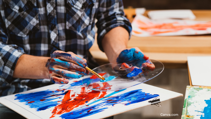 mains d'hommes recouvertes de peinture et prenant au pinceau de la couleur sur une pallette pour peindre sa toile